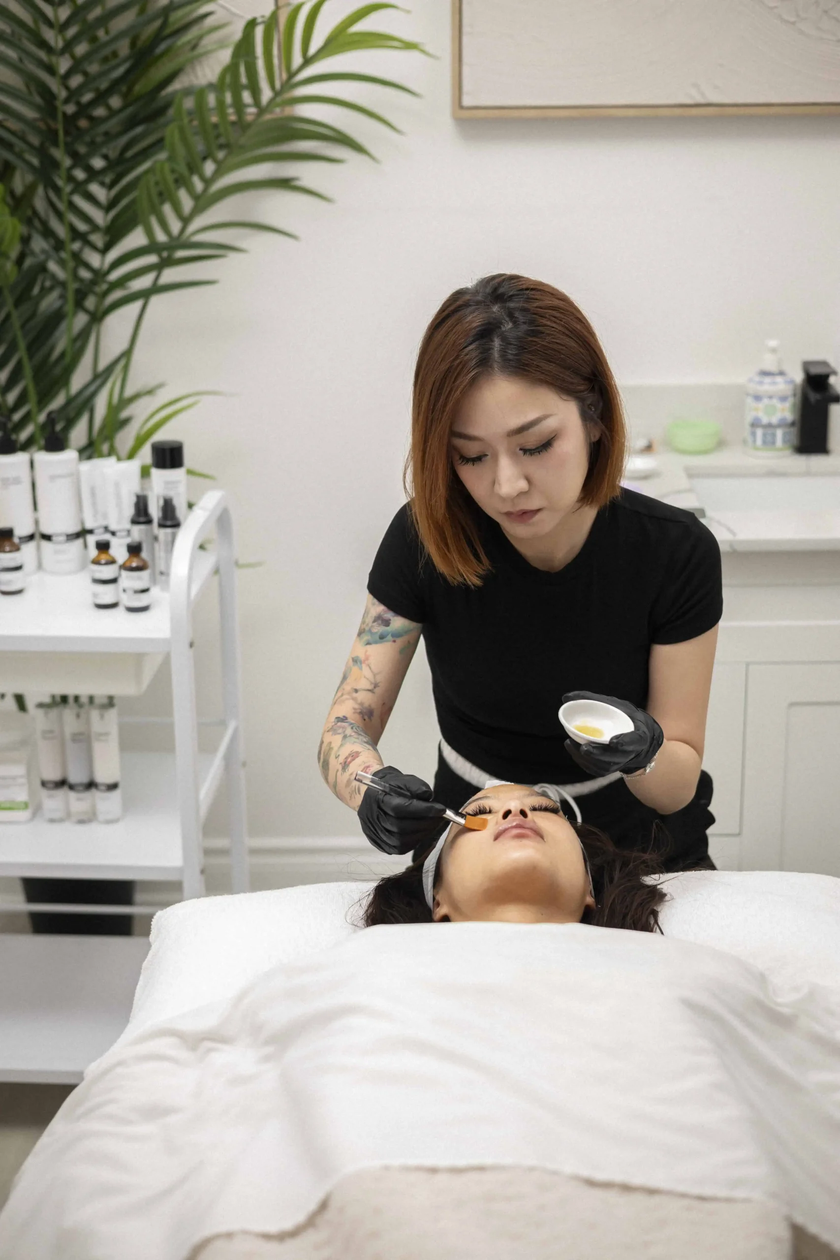 Aesthetician applying facial mask to woman lying in spa bed